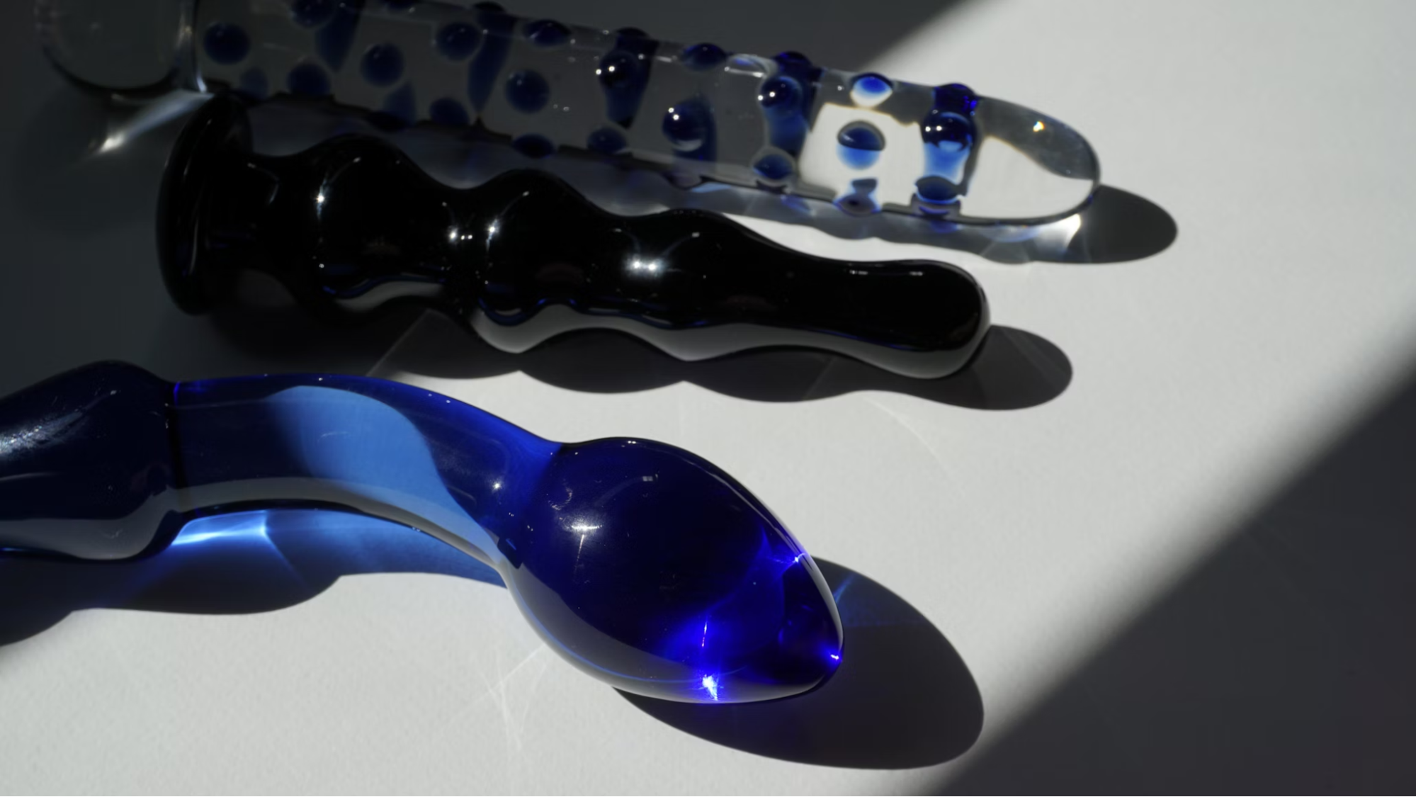 Blue and transparent glass dildos against a white surface