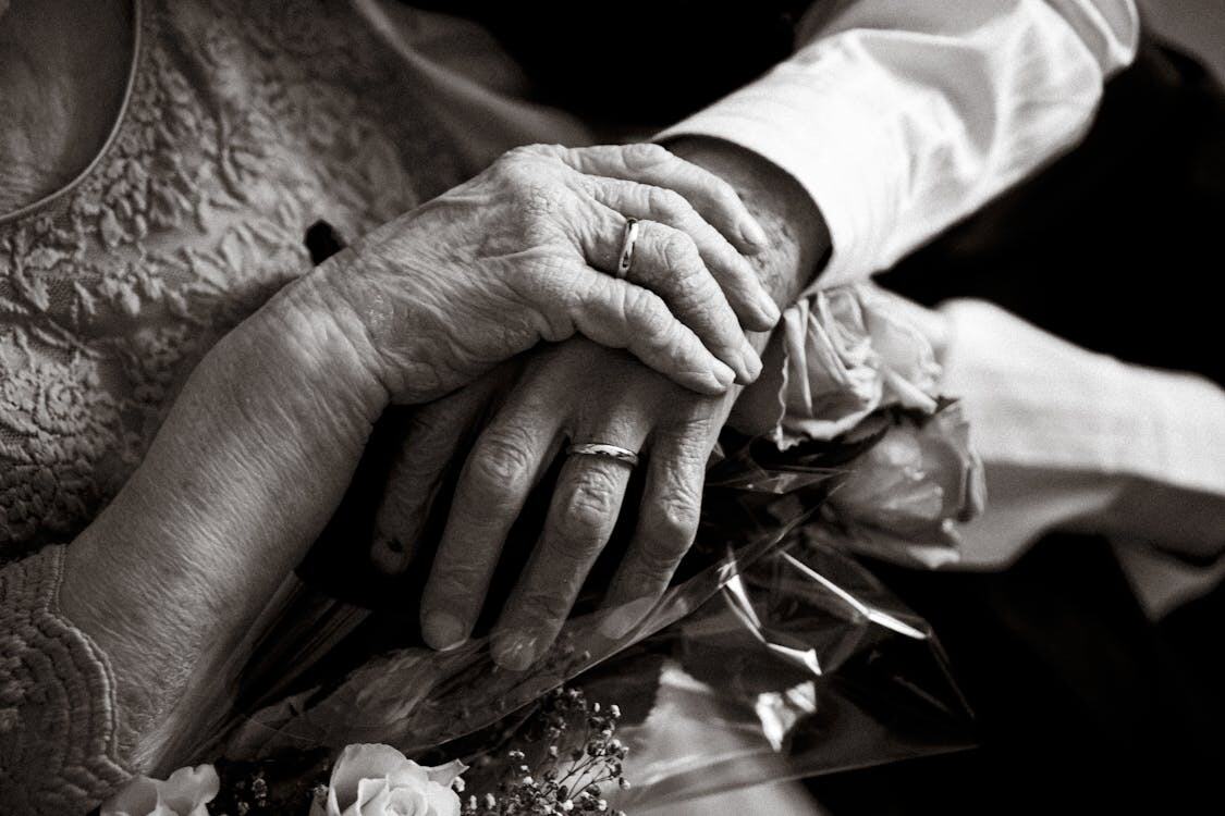 Close-up of clasped, wrinkled hands with wedding bands