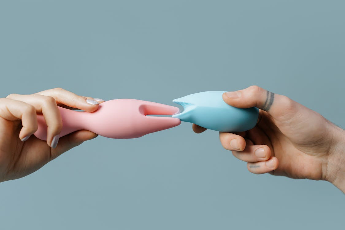 Close-up of hands holding blue and pink silicone sex toys together