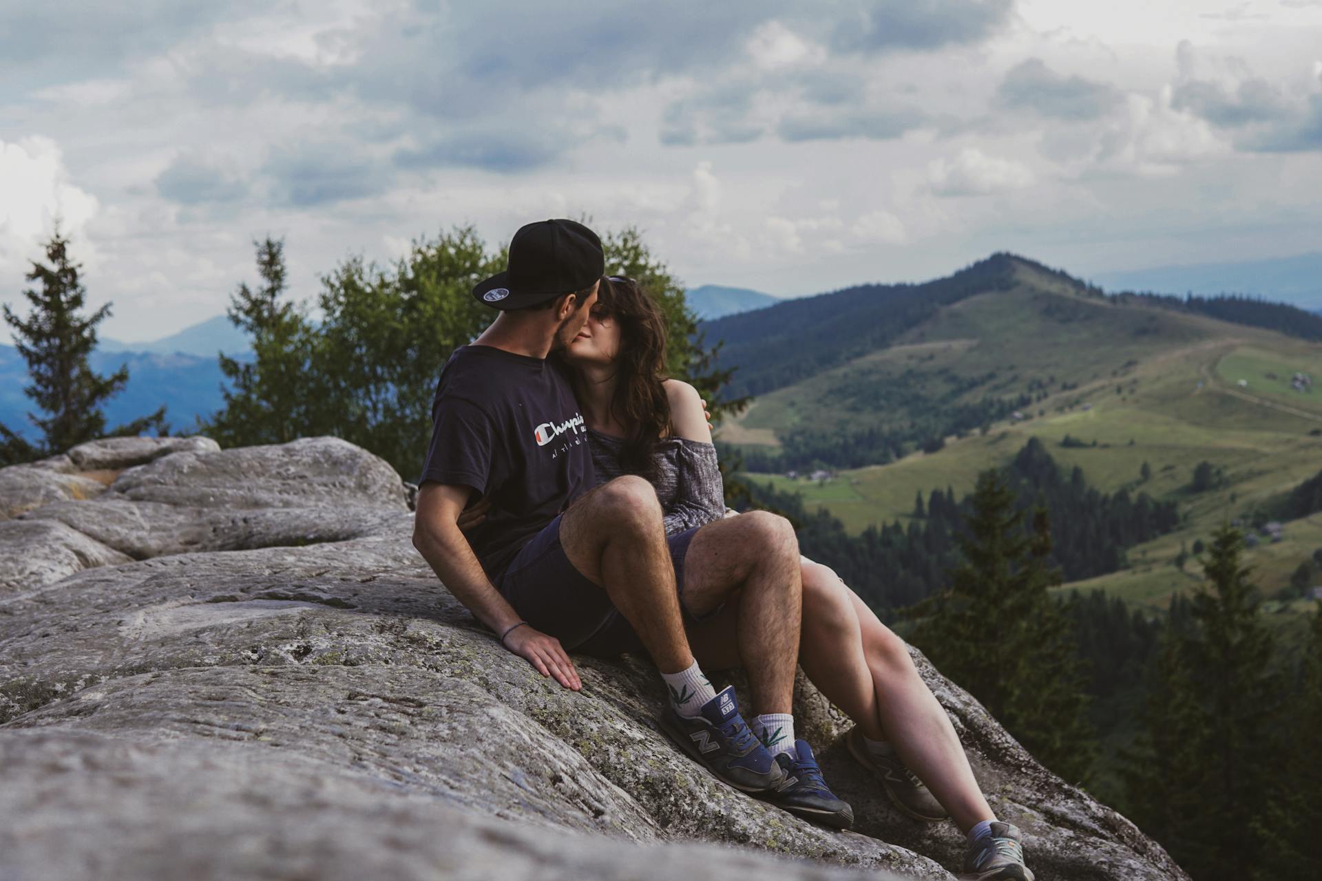 A couple kissing on a rock on top of a mountain