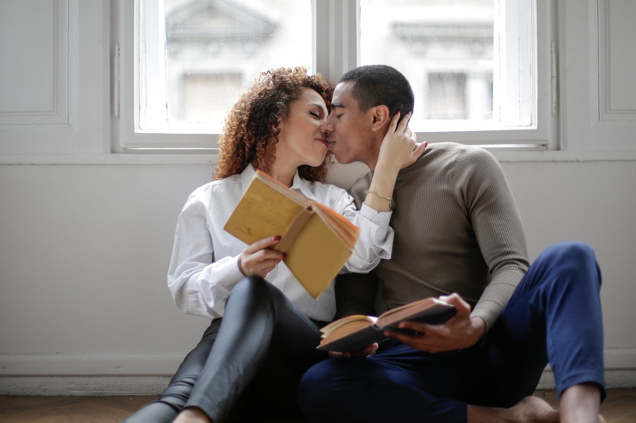 A couple kissing underneath a window while holding novels