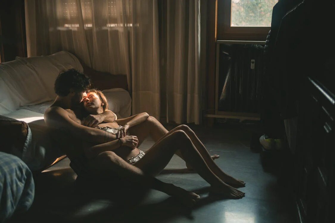 A man and a woman sitting on the floor in a cozy room with dim lighting