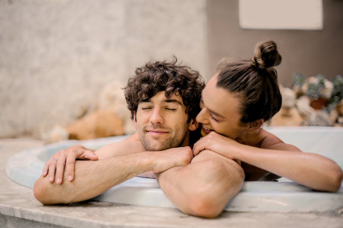 A smiling couple resting on the ledge of a bathtub